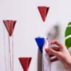 Hand placing a white cloth on a blue PAPERHANK wall hook among a series of red hooks on a white wall, demonstrating their practical use.