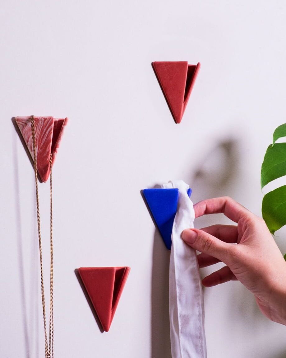 Hand placing a white cloth on a blue PAPERHANK wall hook among a series of red hooks on a white wall, demonstrating their practical use.