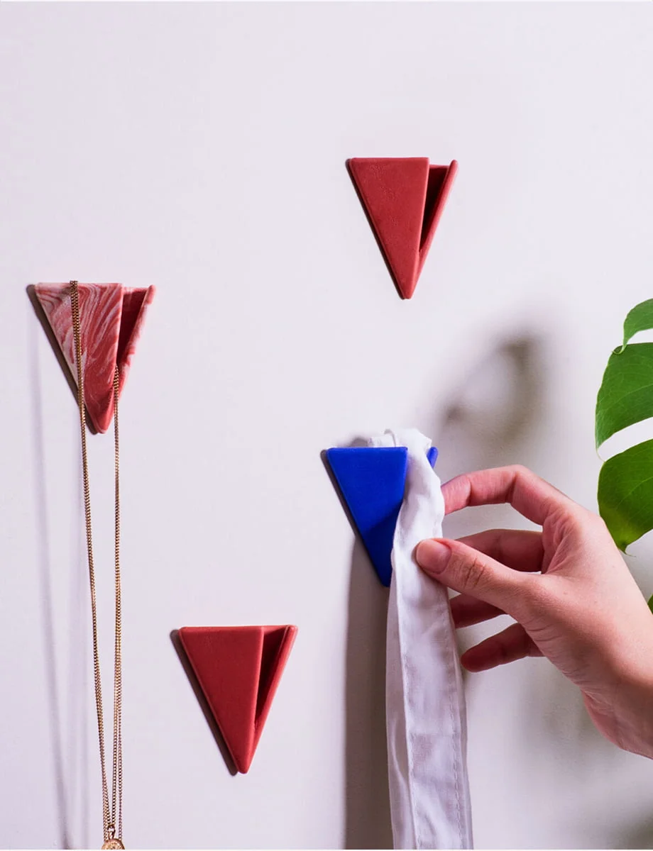 Hand placing a white cloth on a blue PAPERHANK wall hook among a series of red hooks on a white wall, demonstrating their practical use.