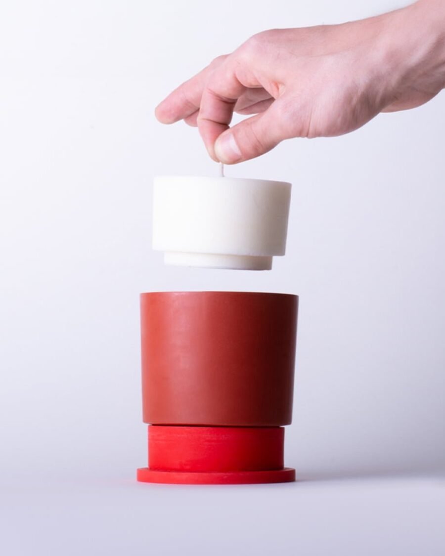 Hand demonstrating the easy refill system of the Poly candle, inserting a new candle into the versatile red Jesmonite holder