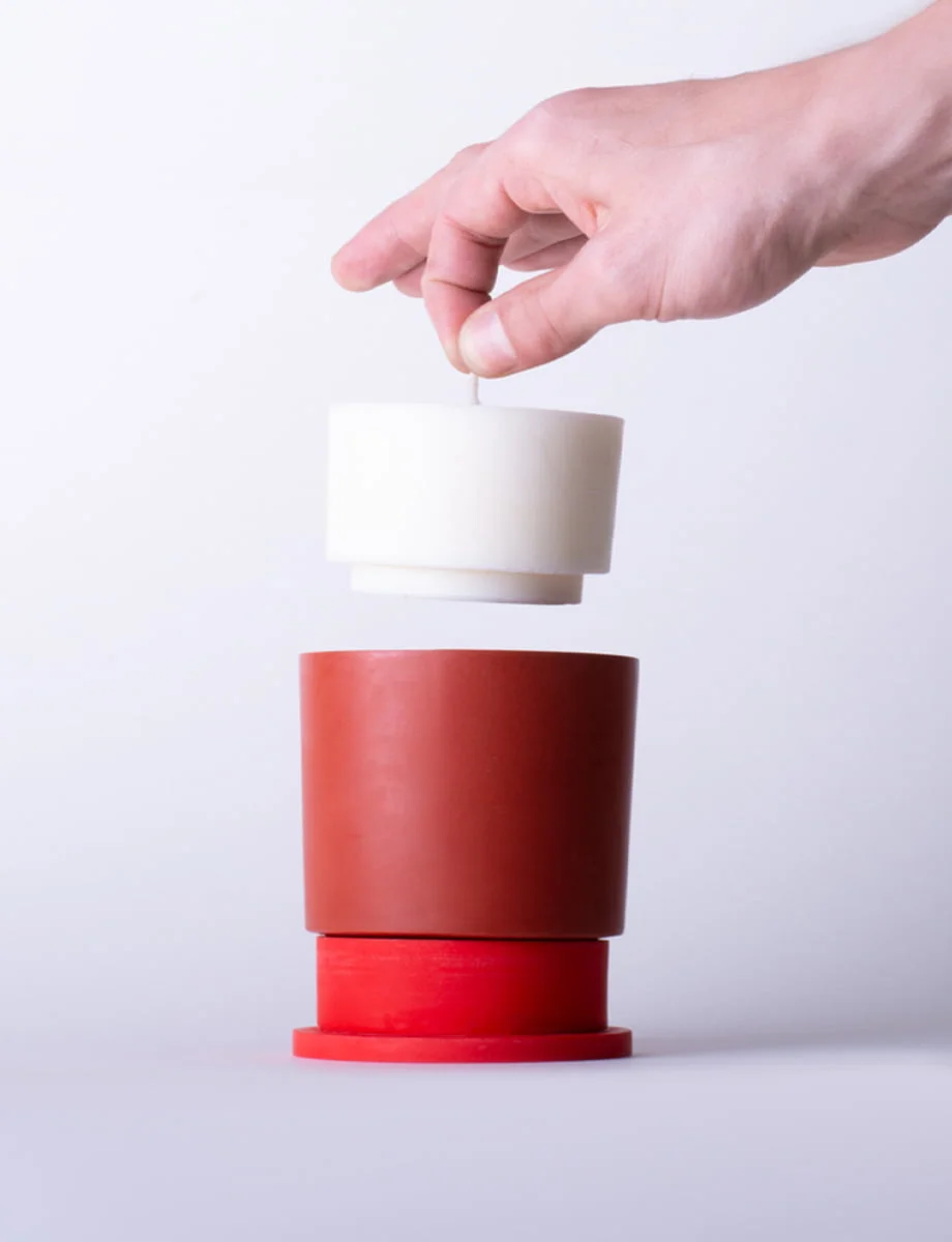 Hand demonstrating the easy refill system of the Poly candle, inserting a new candle into the versatile red Jesmonite holder